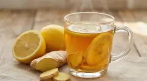 Tisana calda allo zenzero e limone in tazza di vetro con fette di limone e radice di zenzero su tavolo